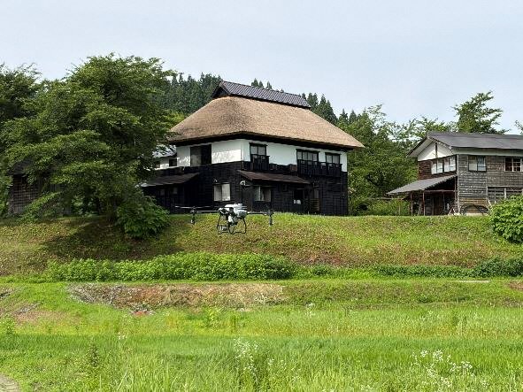 かやぶき民宿の前を飛ぶドローン